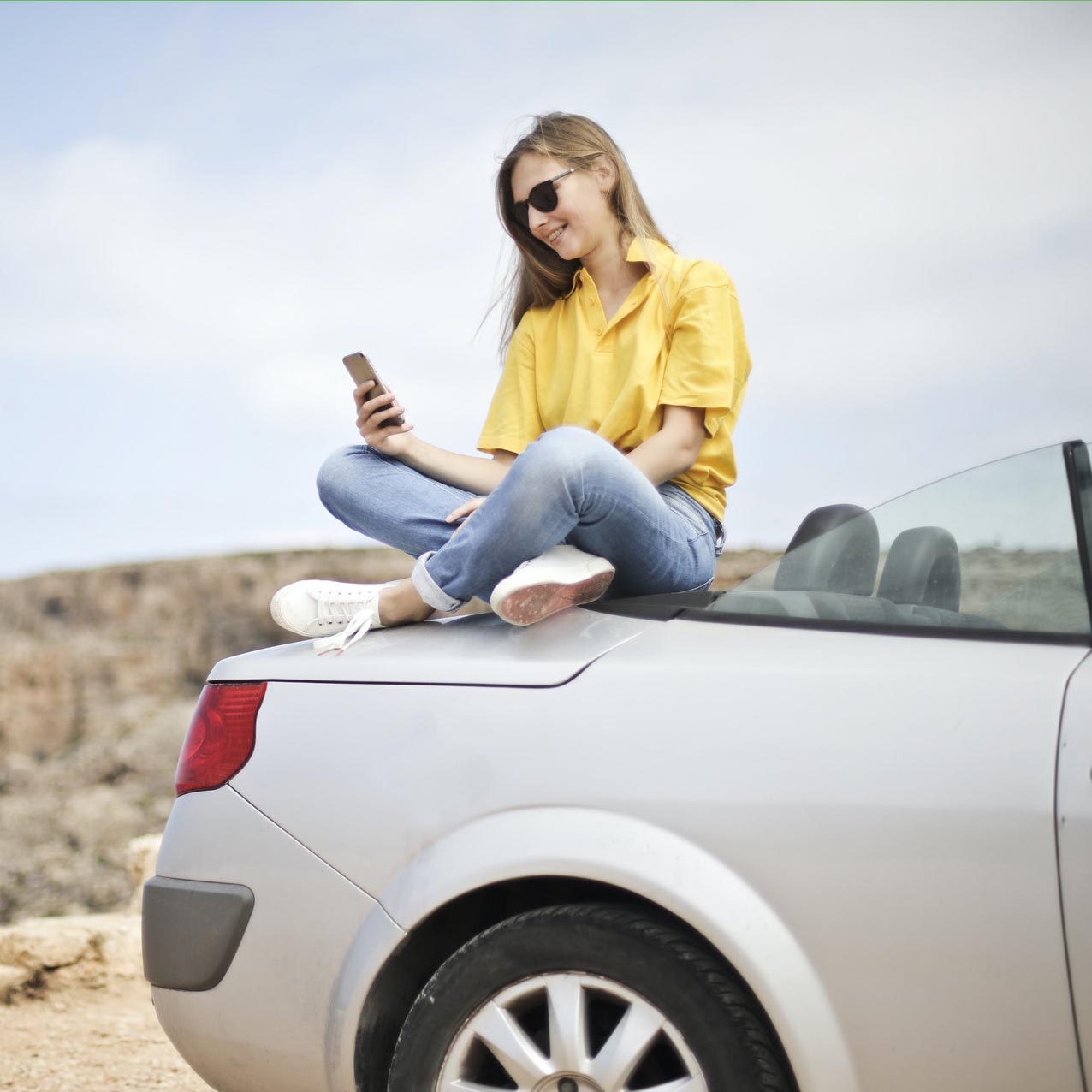 Woman sitting on the back of a convertible using her cell phone